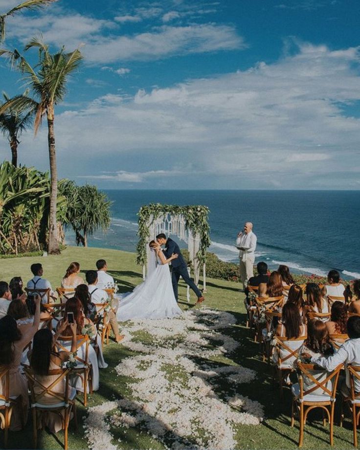 A couple kissing at Bali beach witnessed by officiating minister and sitting wedding guests