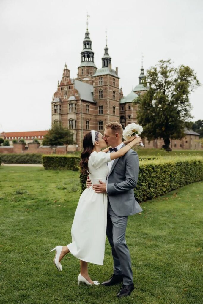 Bride captured in a one-legged pose as she kisses the groom in front of the Rosenburg Copenhagen, Denmark