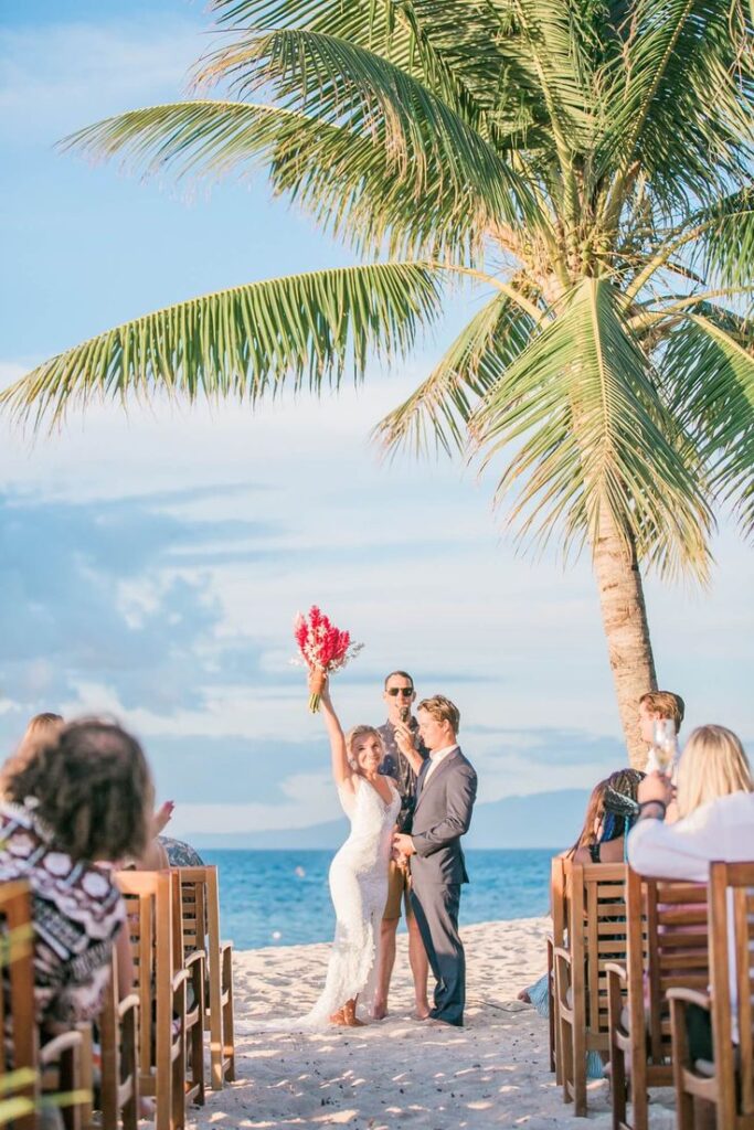 Fiji beach wedding ceremony on a private island with bride joyfully holding up her red bouquet