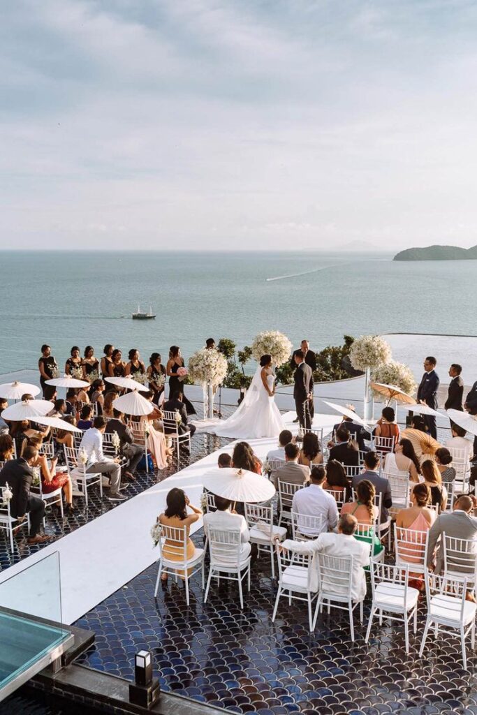 Glamorous Phuket beach wedding with couple standing on the altar and bridesmaids dressed in black gowns