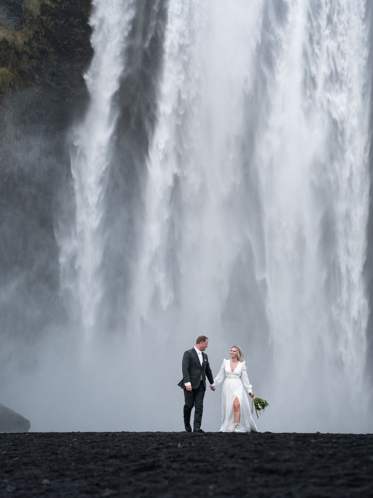 Smiling couple standing before Skógafoss waterfall in Southern Iceland